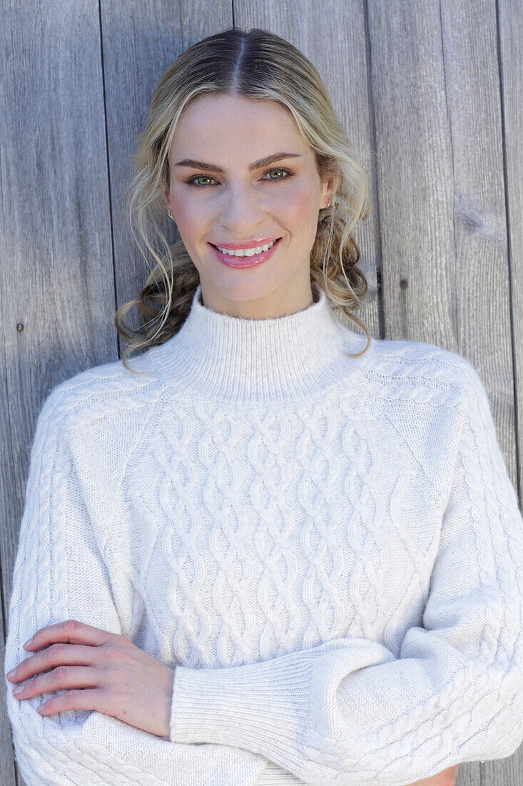 Young blond woman in white knitted jumper in front of board wall