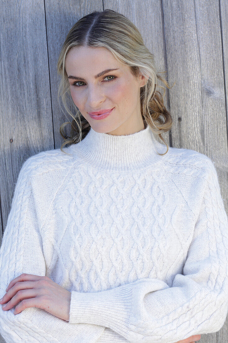 Young blond woman in white knitted jumper in front of board wall