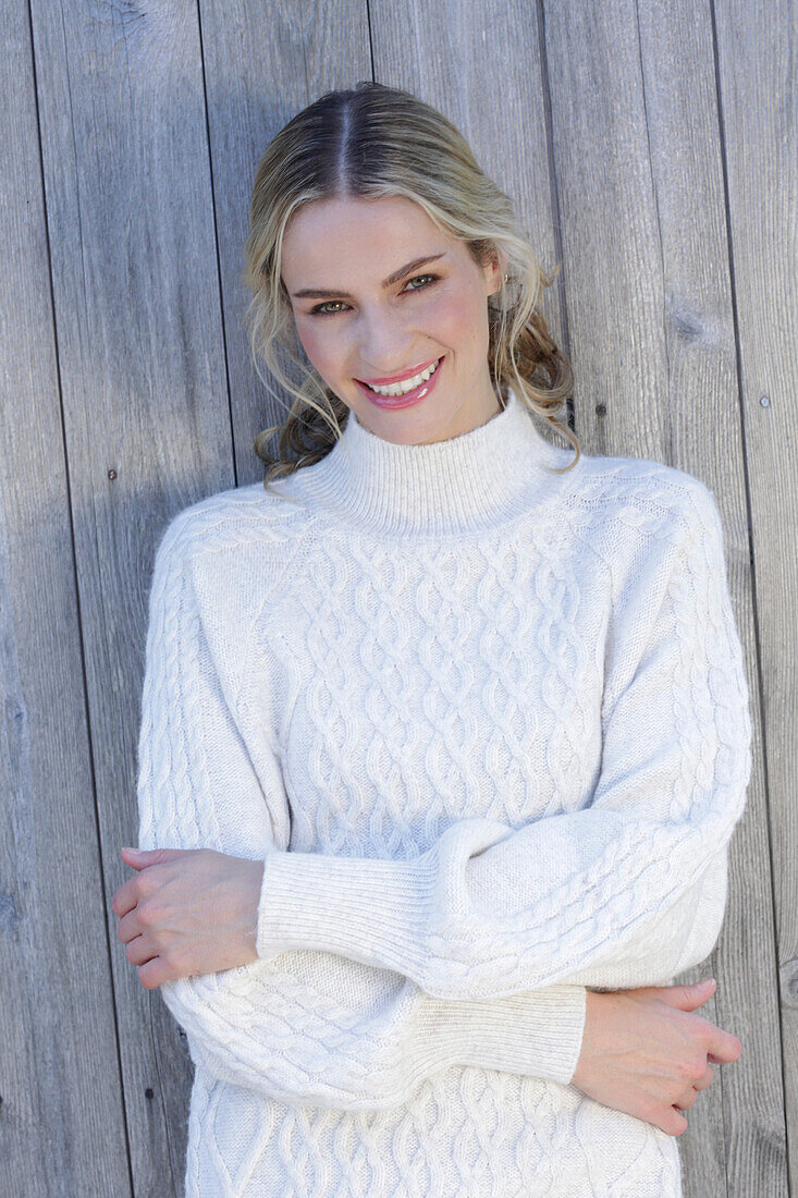 Young blond woman in white knitted jumper in front of board wall