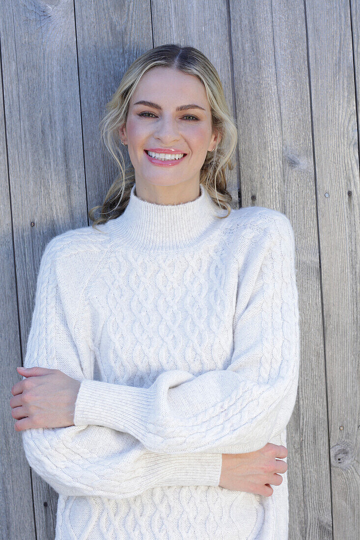 Young blond woman in white knitted jumper in front of board wall