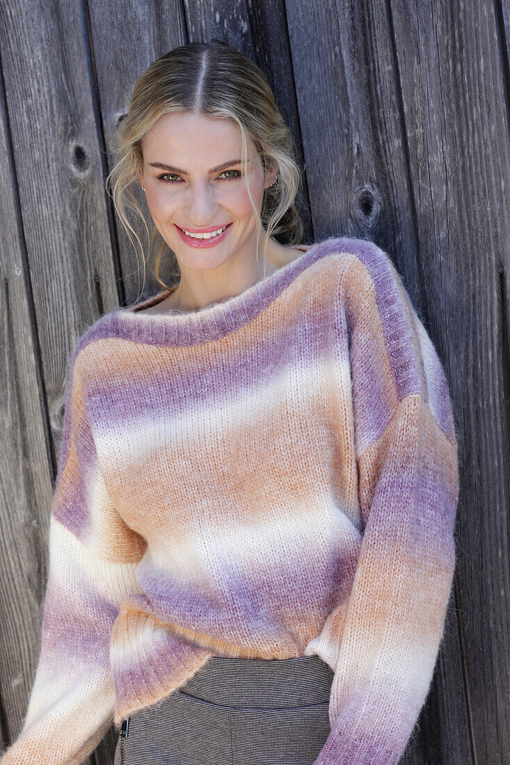 Young blond woman in knitted jumper with colour gradient in front of board wall