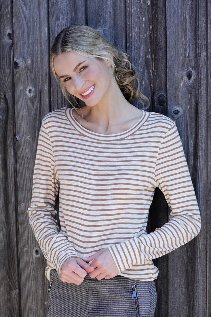 Young blond woman in striped shirt in front of board wall