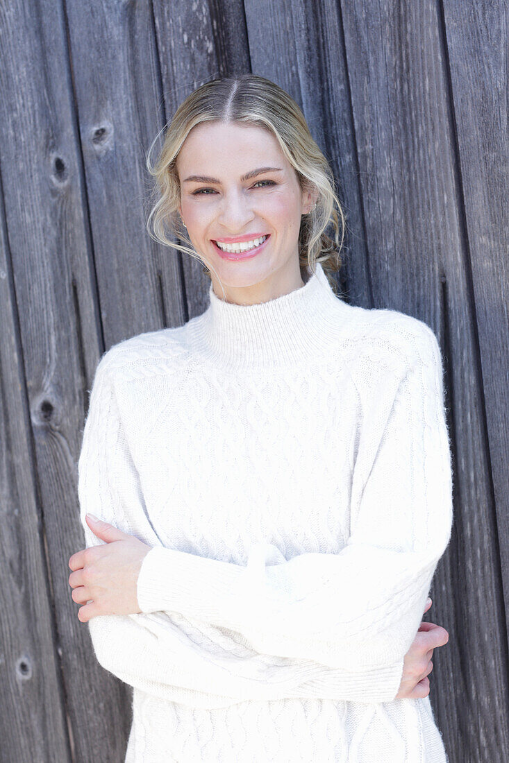 Young blond woman in white knitted jumper in front of board wall