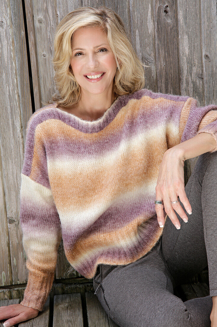 Mature blonde woman in knitted jumper with colour gradient and grey leggings