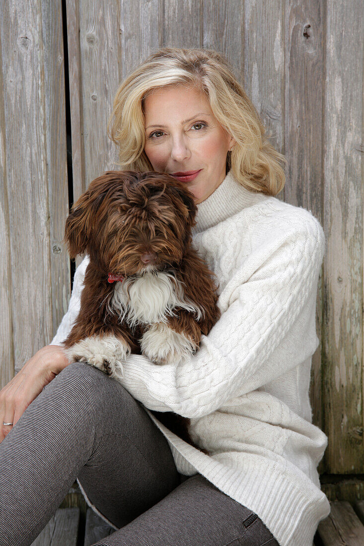 Reife blonde Frau mit Hund in weißem Strickpullover und grauen Leggins