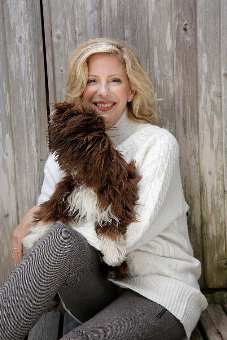 Mature blonde woman with dog in white knitted jumper and grey leggings