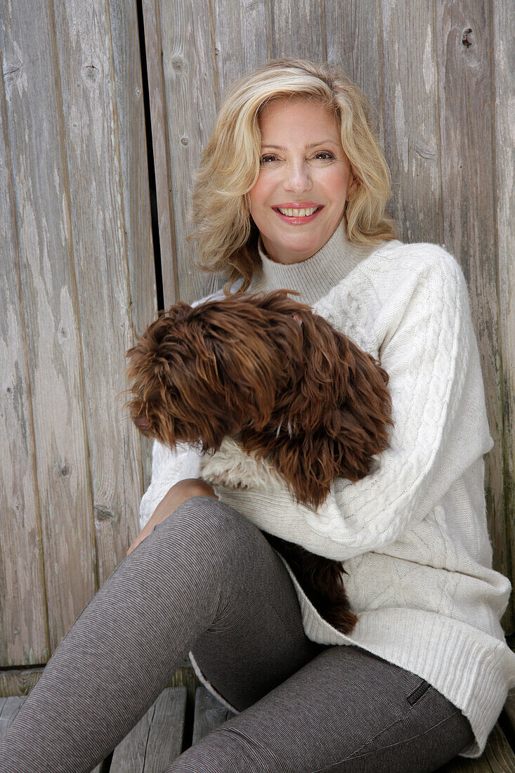Reife blonde Frau mit Hund in weißem Strickpullover und grauen Leggins