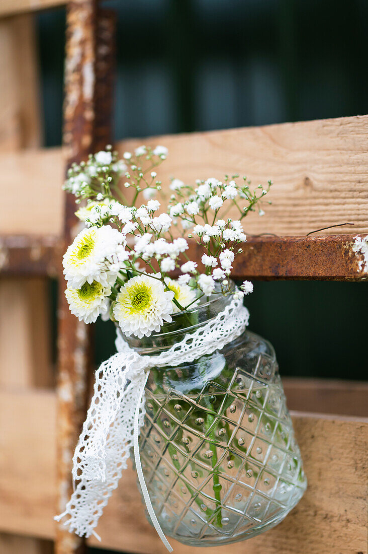 Weisse Blumen mit gelber Mitte und Schleierkraut hängen in einem Glas an einer Palette