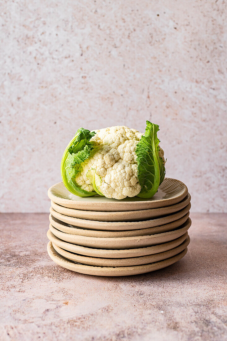Organic cauliflower with leaves on a stack of fluted ceramic plates