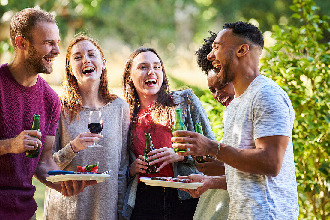 Fröhliche junge Freunde, die im Garten gemeinsam essen und trinken