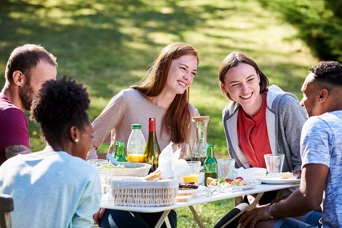 Lächelnde junge Freunde, die Essen im Garten genießen