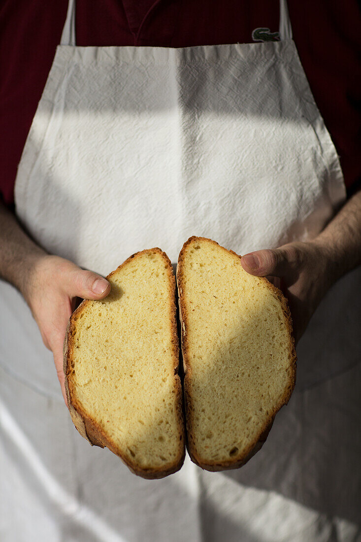 Bäcker hält halbiertes Pane di Altamura (italienisches Hartweizenbrot) in den Händen