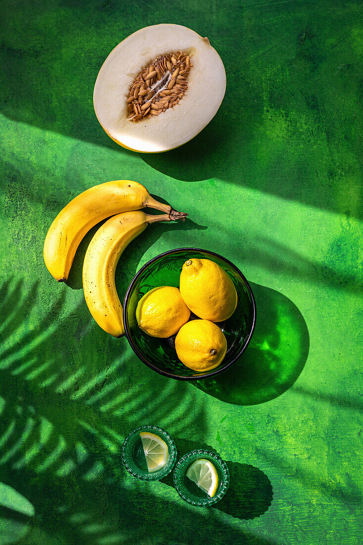 Zitronen, Bananen und Galiamelone auf grünem Untergrund