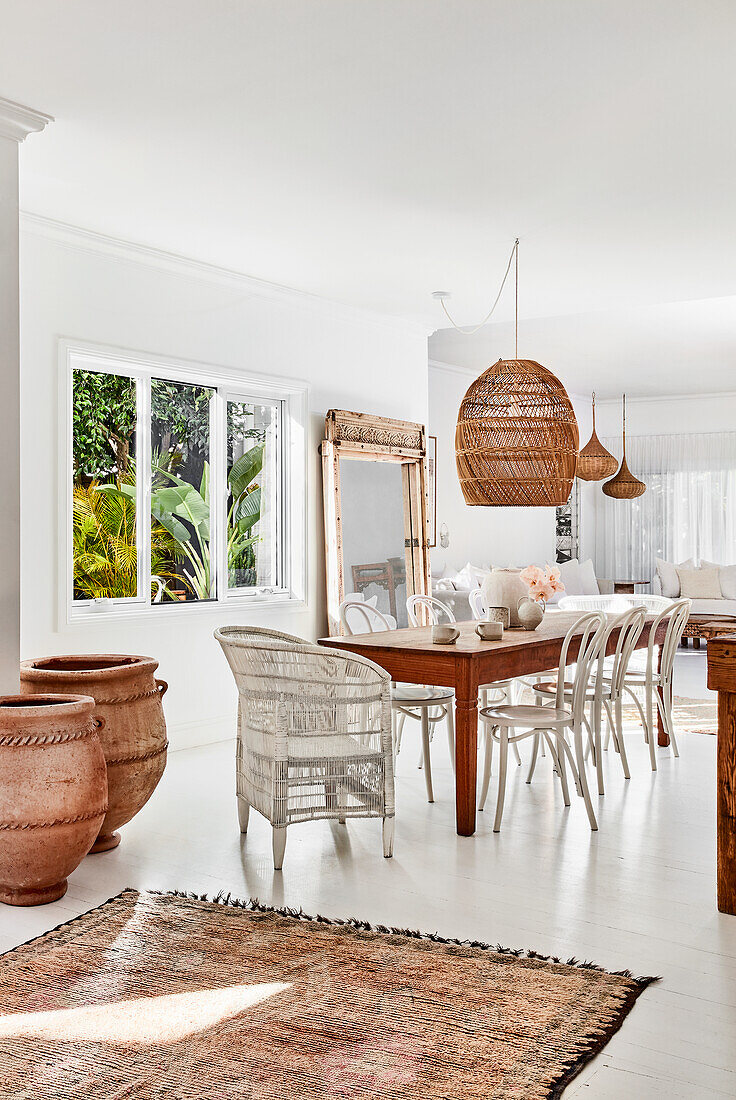 Rustic wooden dining table with white chairs, rattan lamp above in dining room