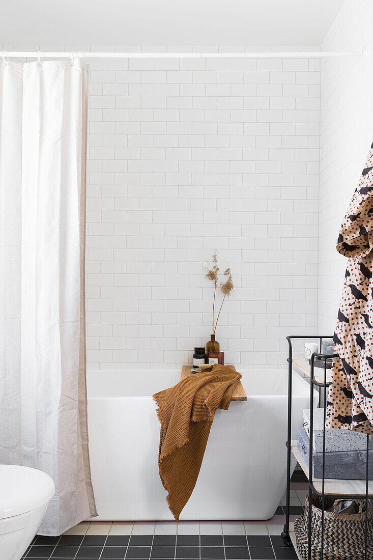 Bathtub and shower curtain in front of white tiled wall in a bathroom