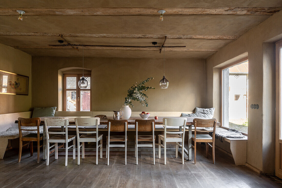 Long wooden dining table with bench and chairs in a rustic room in earth tones