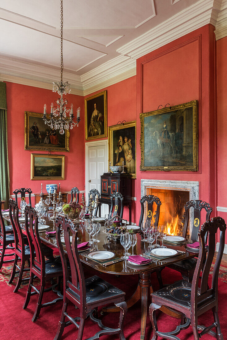 Festively set table in front of fireplace with burning fire, collection of paintings on red walls