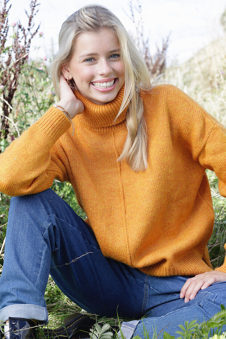 Junge blonde Frau in gelbem Rollkragenpullover und Jeans in der Natur