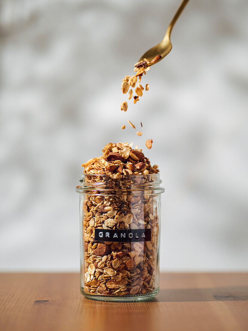 Granola pouring from spoon to glass jar