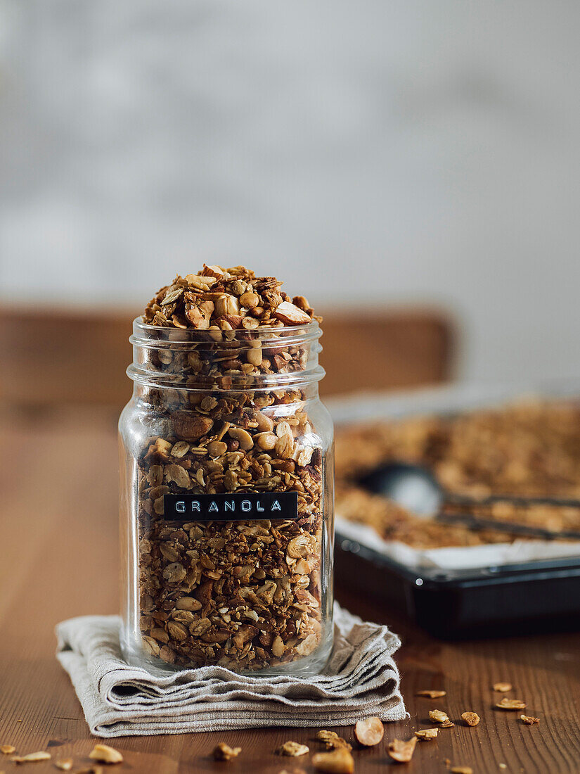 Homemade granola in glass jar near cooking tray on wooden table