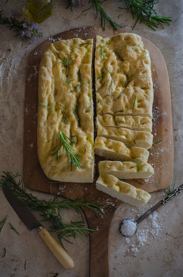 Easy recipe rosemary focaccia on a wooden cutting board, decorated with rosemary