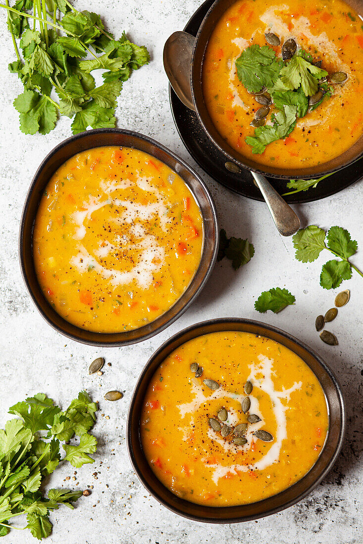 Three bowls of carrot soup with various garnishes including coconut milk, pumpkin seeds and fresh ciriander