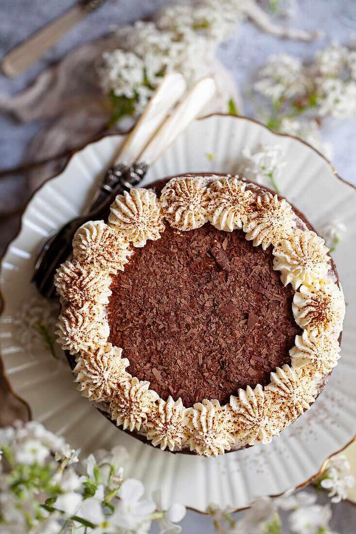 Overhead view of a chocolate cake decorated with whipped cream, chocolate flakes and cocoa powder