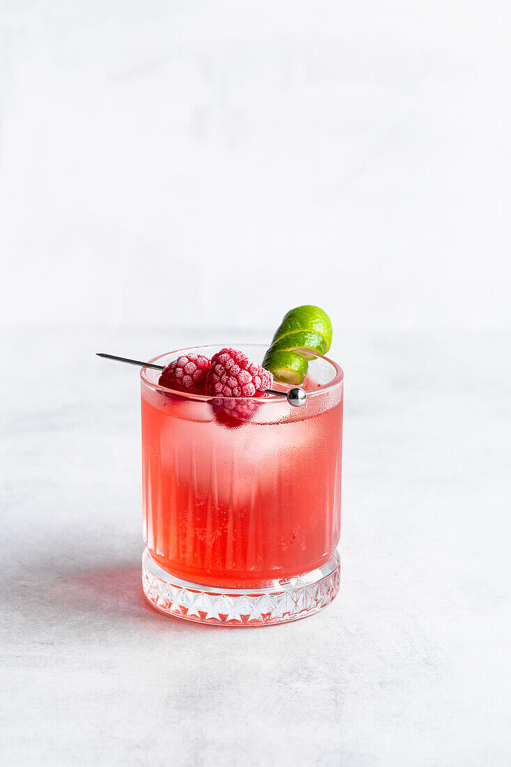Raspberry and lime cocktail with frozen raspberries and lime garnish