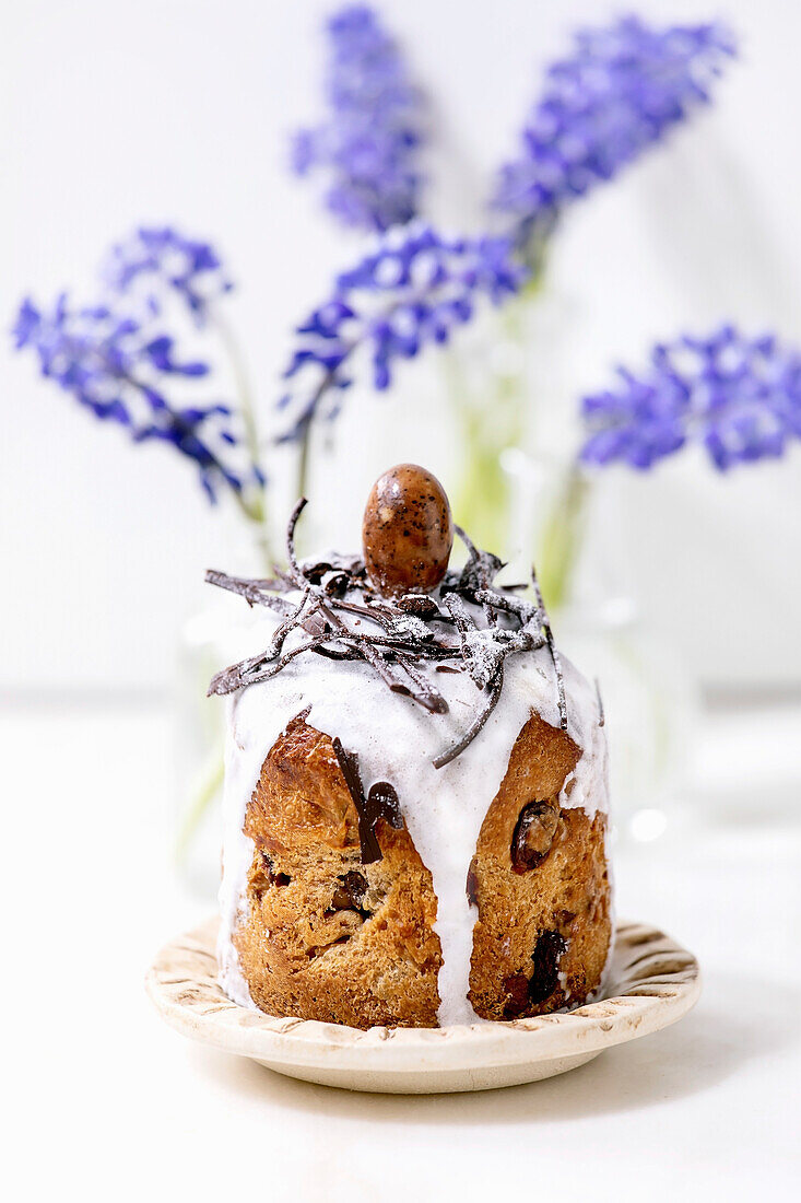 Homemade traditionla Easter kulich cake with chocolate nests and eggs on ceramic plates decorated with muscari flowers