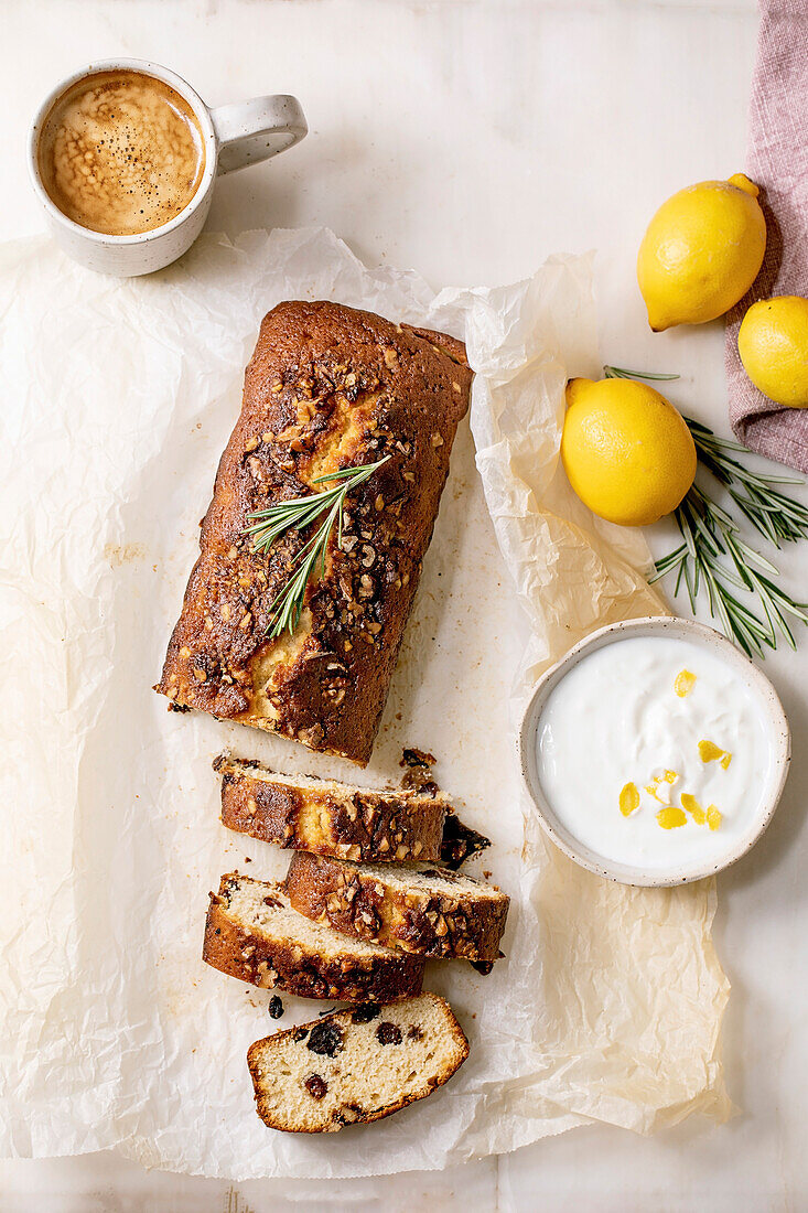 Sliced homemade lemon cake with raisins, nuts and rosemary on crumpled baking paper