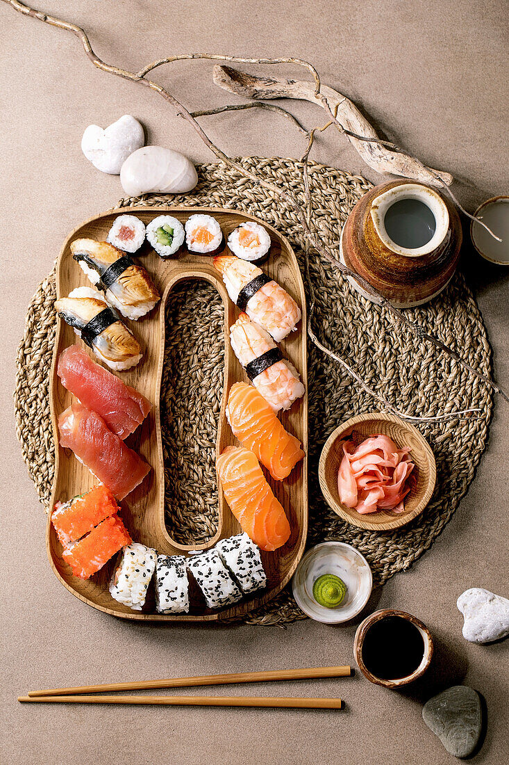 Sushi rolls set. Traditional japanese dish sushi and rolls with fresh salmon, tuna, eel and prawns on rice. Serving on wooden plate with soy sauce, sake and stones on brown background. Flat lay.