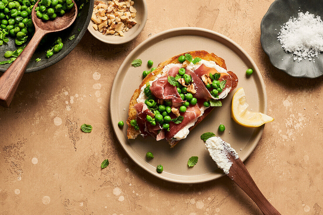 Crostini mit Ricotta, Prosciutto und Erbsen daneben Walnüsse und Meersalzflocken