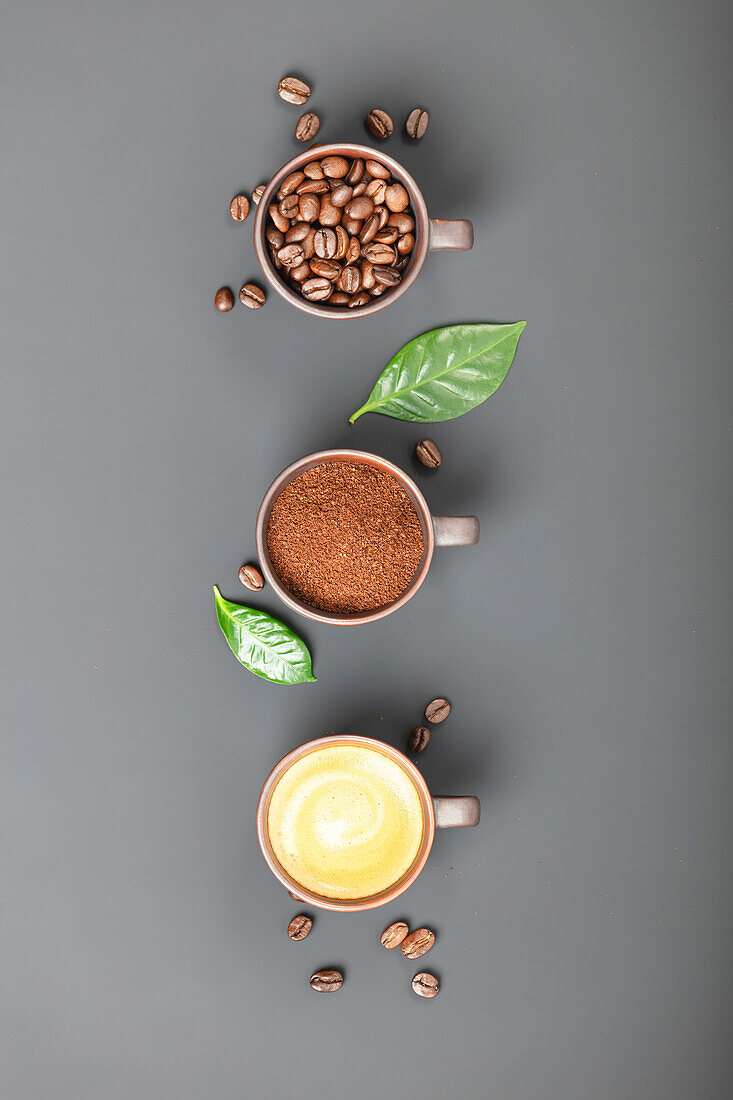 Kaffeebohnen, Kaffeepulver und aufgebrühter Kaffee in Tassen auf grauem Untergrund