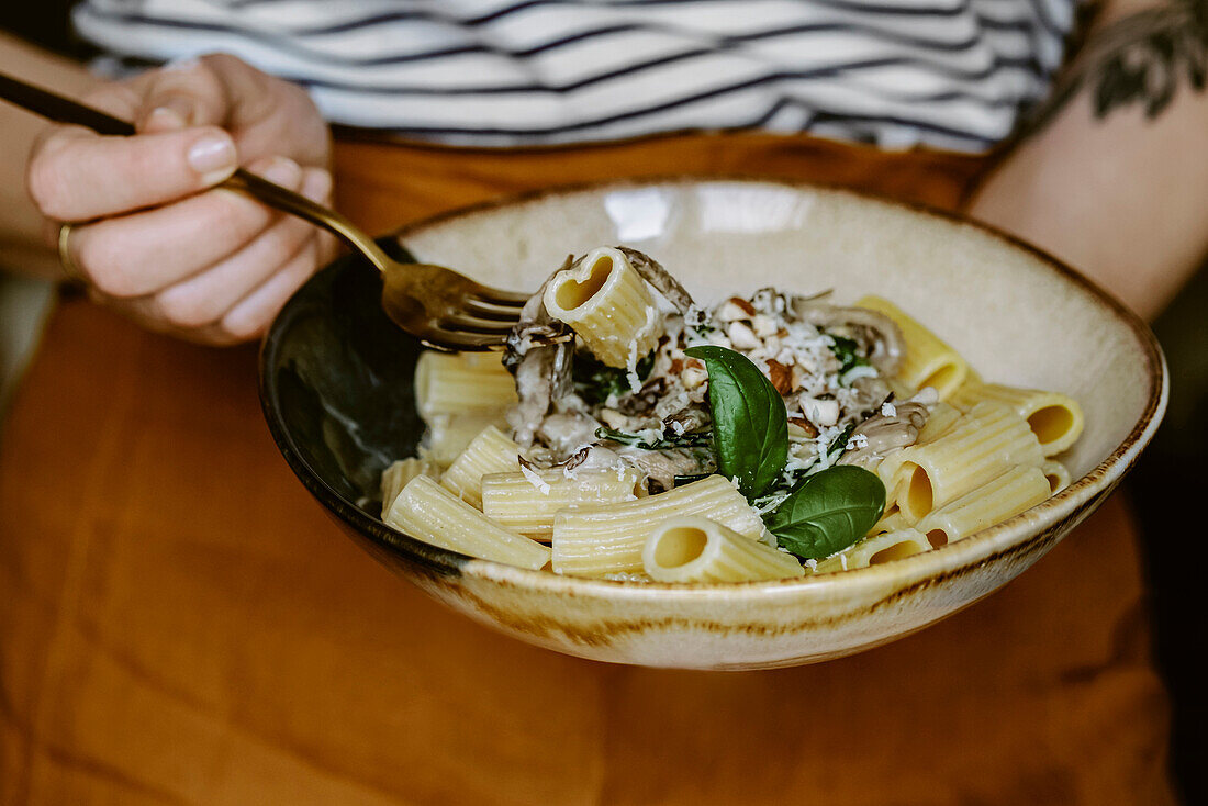 anonymous woman with linen terracota apron, holding a Rigatoni pasta dish, with cream, mushroom, spinach, almond and grated parmesan, in handmade plate