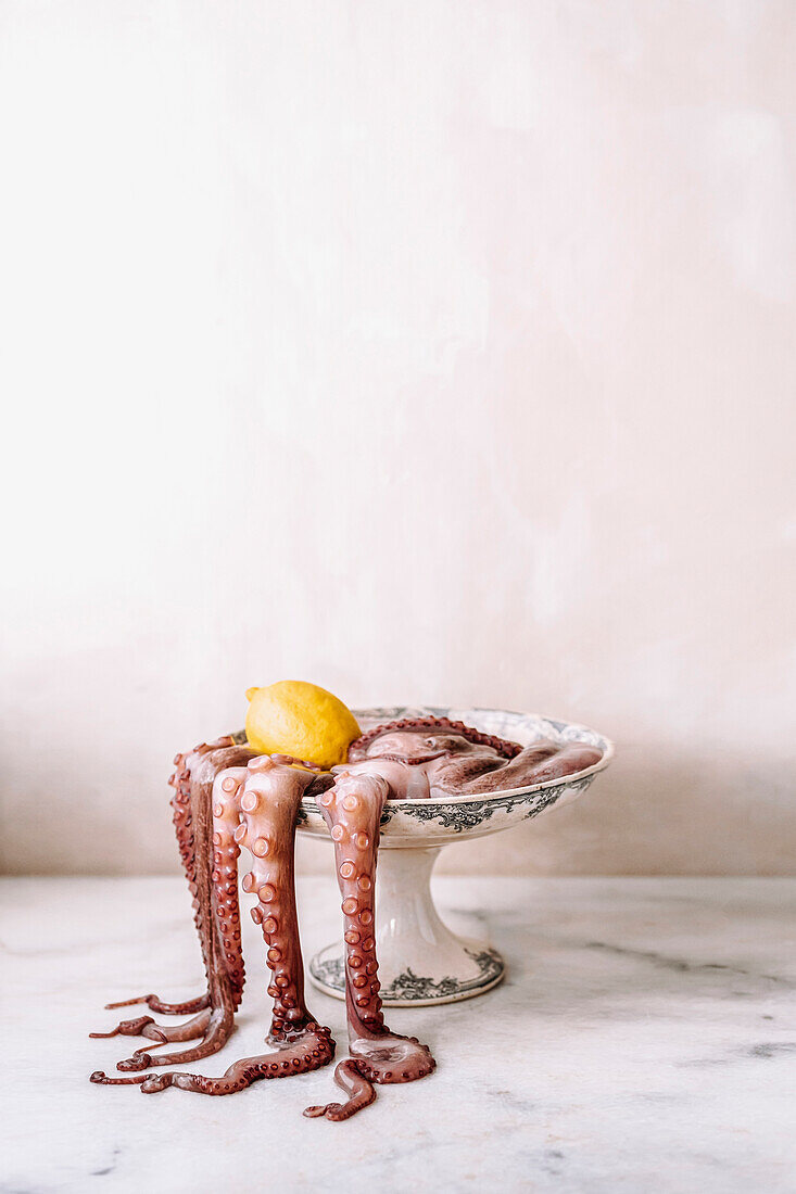 Oktopus mit Tentakeln und Zitrone in Schale eines Vintage-Porzellanständers