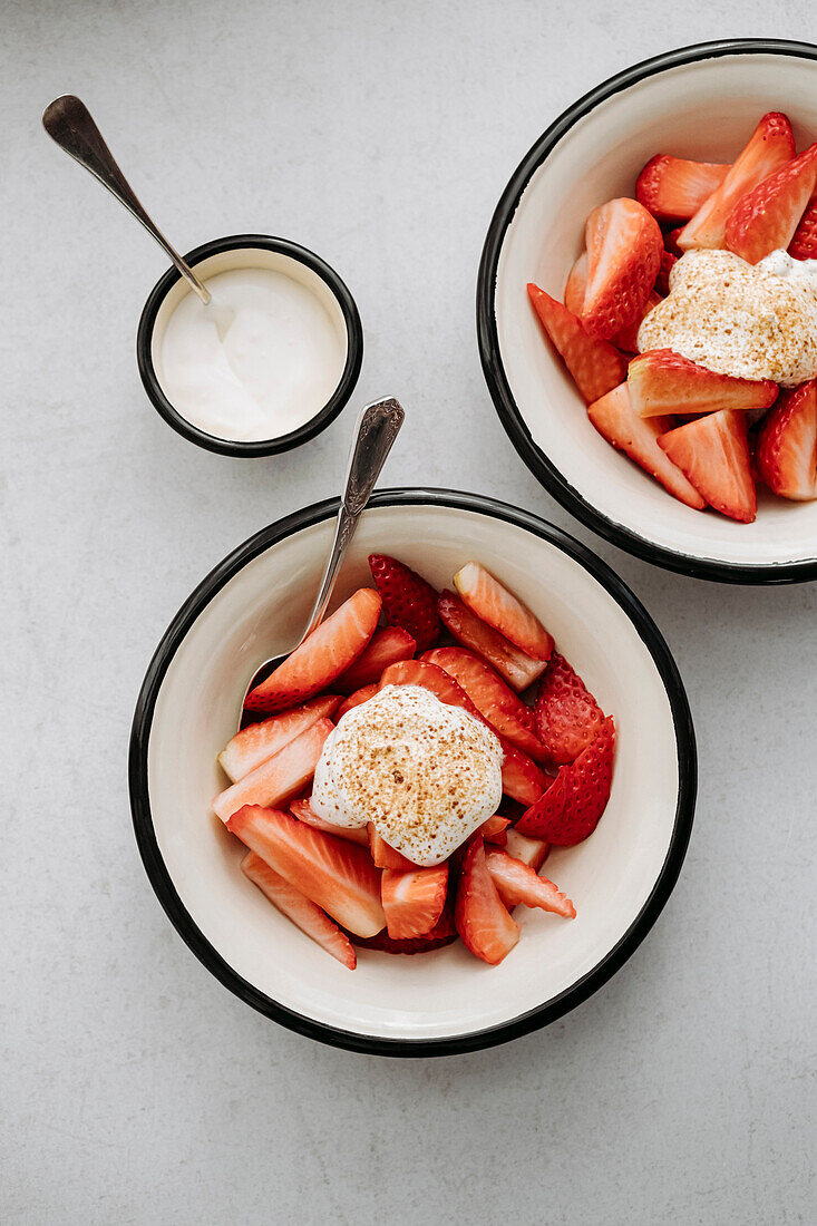 Metal bowl enamelled with slices of fresh strawberries and whipped cream and brown sugar