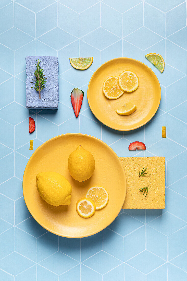 Komposition aus Zitrone auf gelben Tellern mit Erdbeerscheiben und Rosmarinzweigen