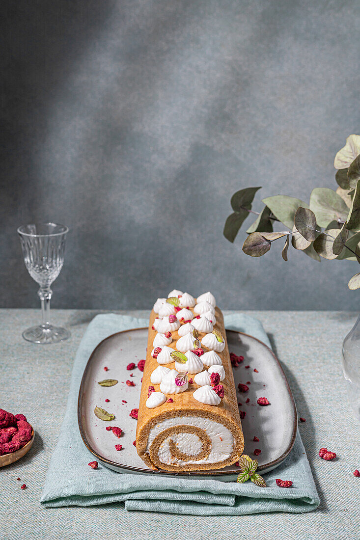 Sweet biscuit roll with cream filling served with dried berries and leaves on plate placed on towel