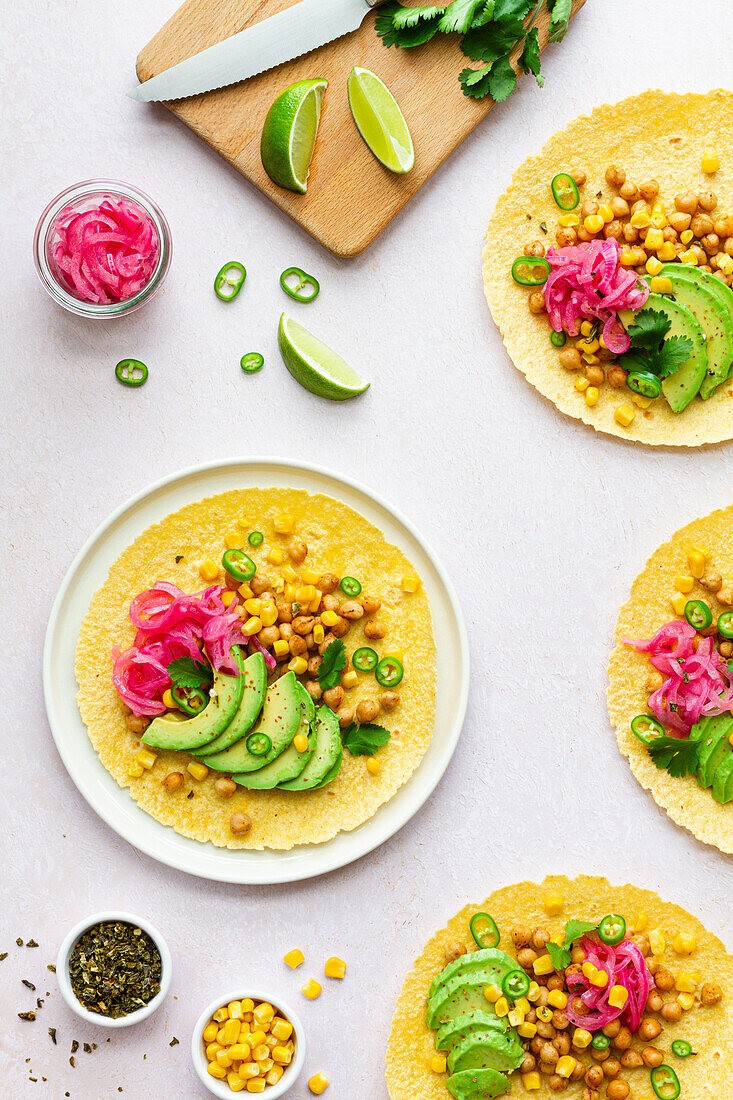 Tortillas with sliced avocados and chickpeas and lime slices and green pepper on white background