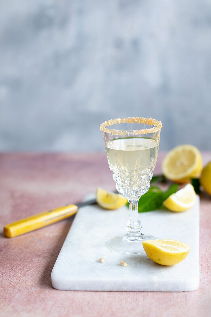 Chalice of citrus cocktail with sugar rim placed on marble board near knife and cut lemons in daytime