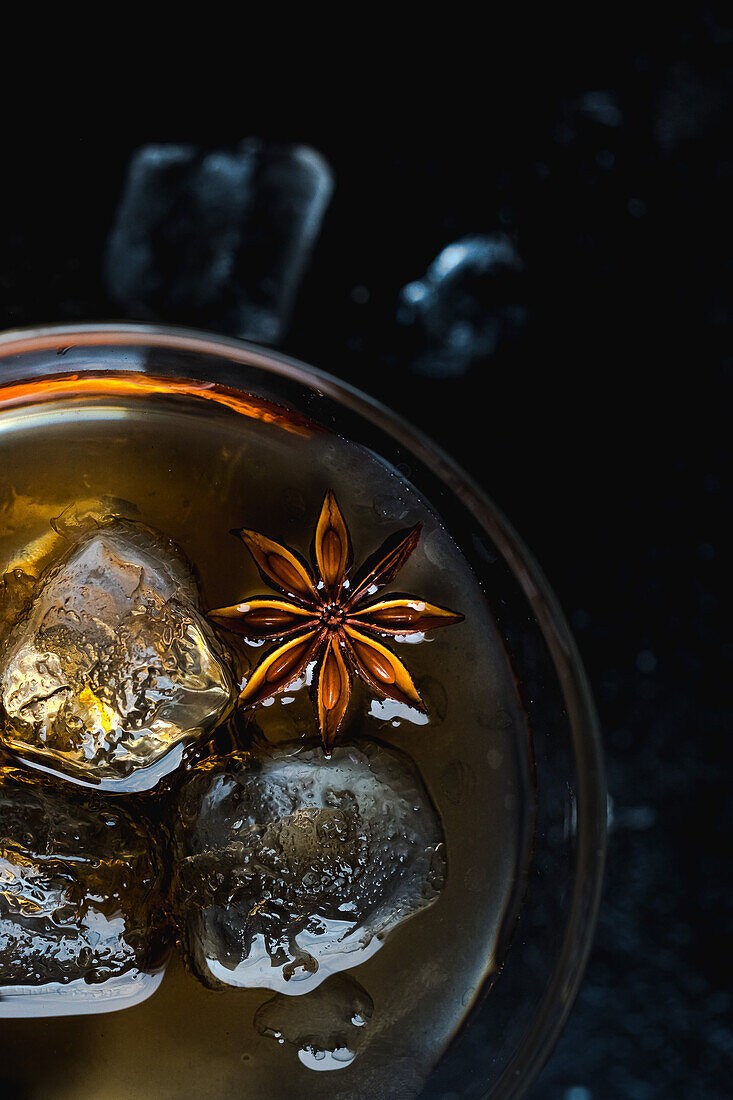 Close-up of glass cup with cold whiskey, cubes of ice and star anise