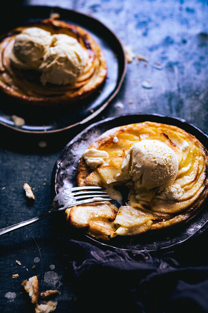 Apple tart with balls of ice cream served on plates with fork on dark marble table