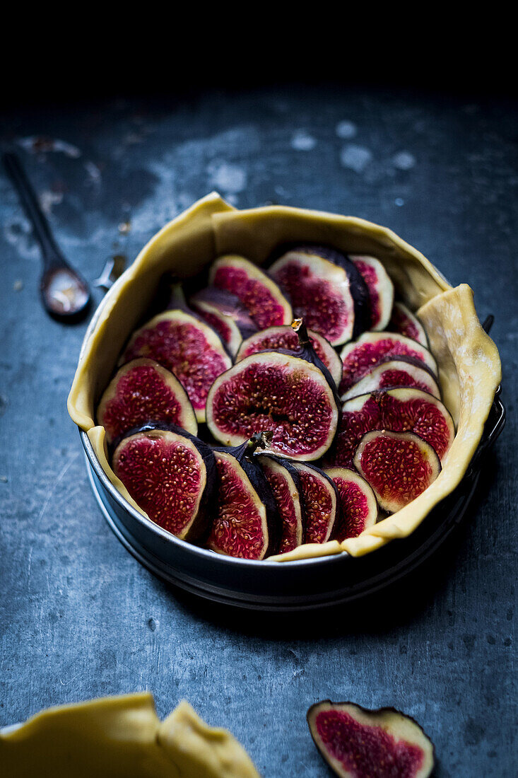 Baking pan with raw dough and slices of figs placed on dark gray table