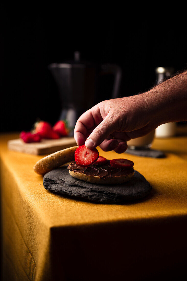Hand placing piece of fresh strawberry on bagel with chocolate paste