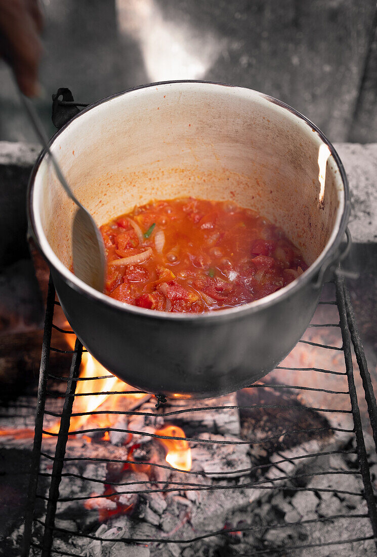 Mexican tomato soup in metal bowler placed on a metal grid over fire and mixed with spoon