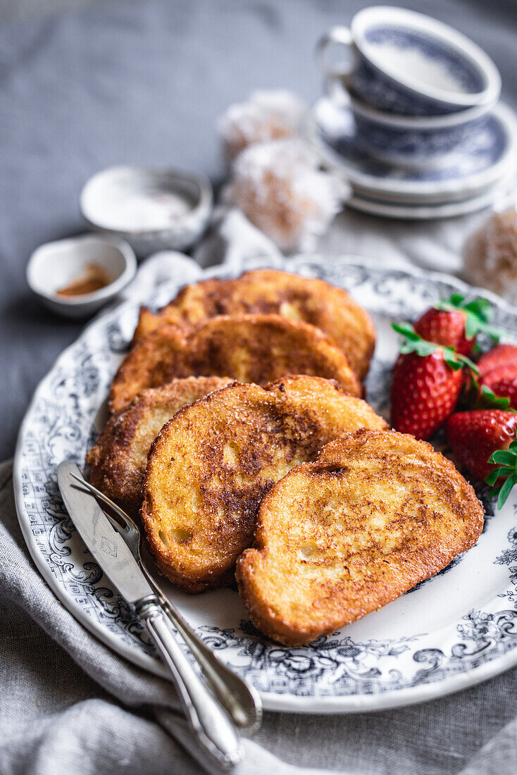 Yummy French toasts with ripe strawberries served on porcelain plate with silverware