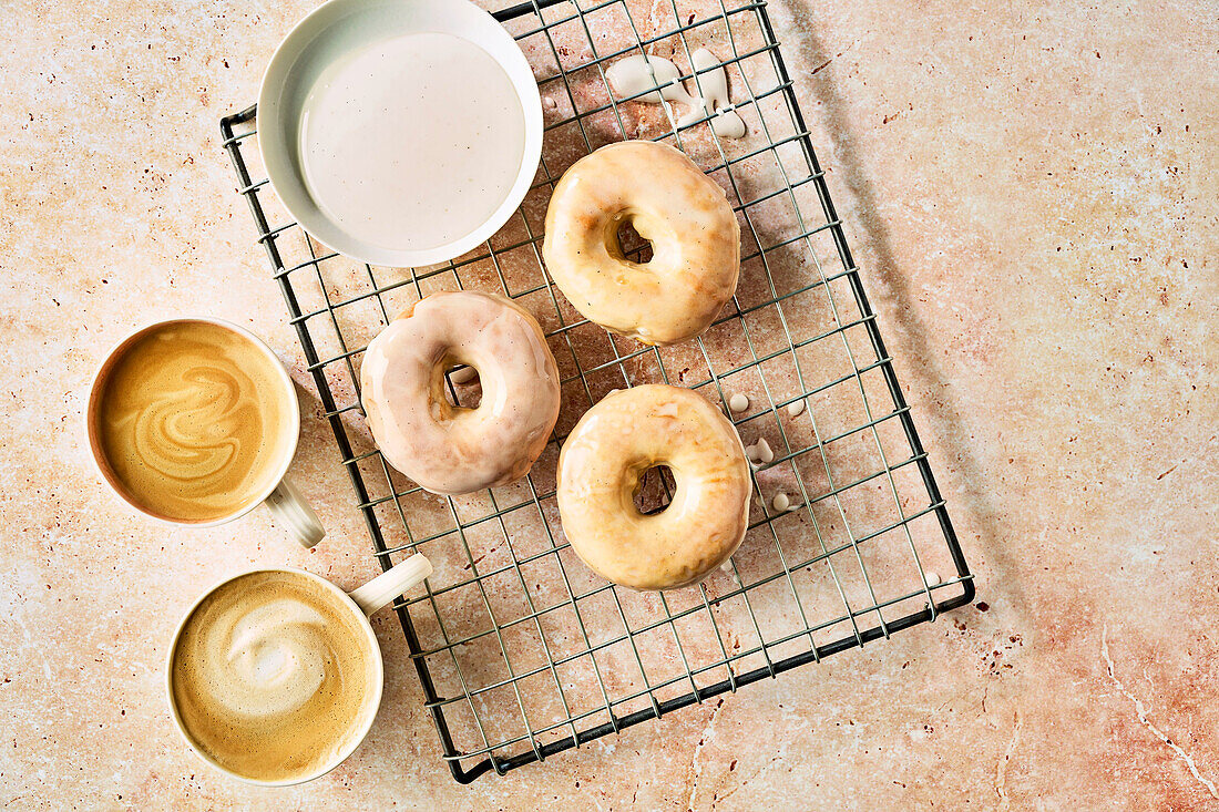 Glasierte Donuts auf Abkühlgitter daneben zwei Tassen Kaffee