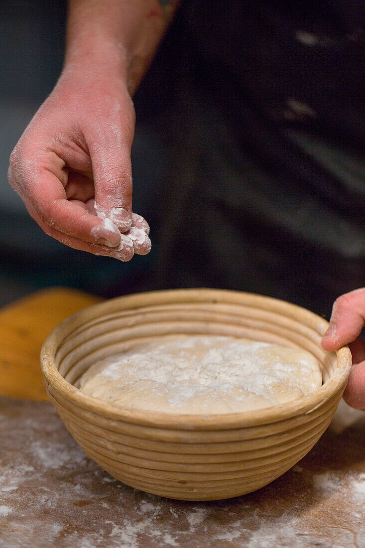 Bäcker streut Mehl auf Brotteig in Gärkorb