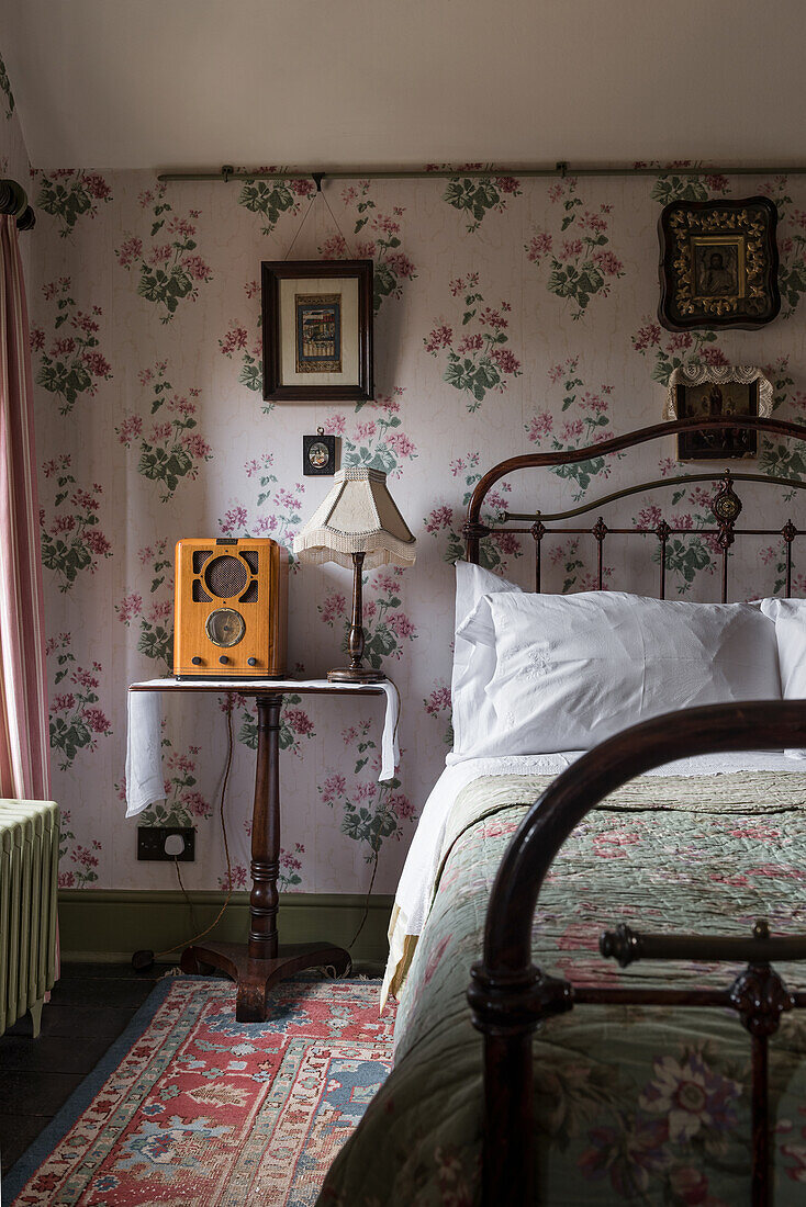 Doppelbett, daneben Vintage-Radio auf Nachttisch im Schlafzimmer mit Blumentapete