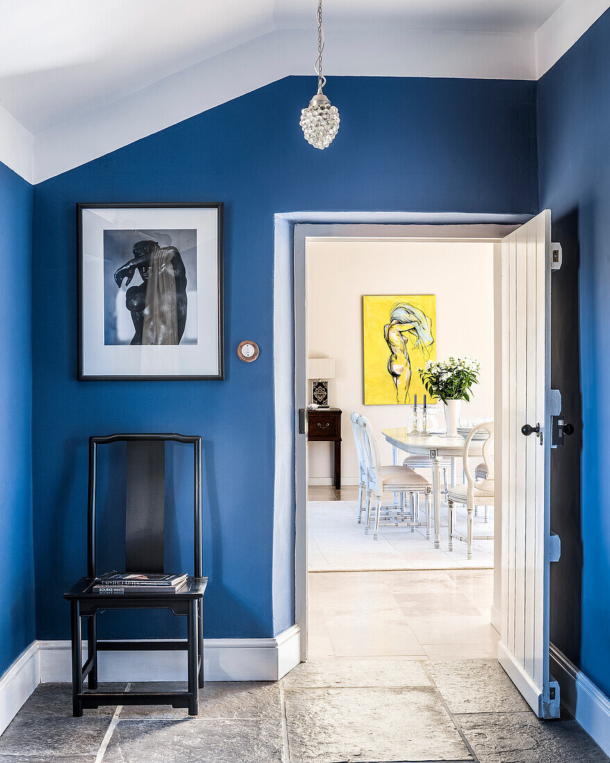 Blick von der Eingangshalle mit blauen Wänden in das helle, lichtdurchflutete Esszimmer mit Gemälde